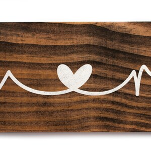 May include: Wooden sign with the words "Home" and "Sweet" written in white cursive script, with a white heart symbol between the words.