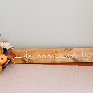 May include: A wooden sign with the text "leanne &hearts; emily" written in white cursive.