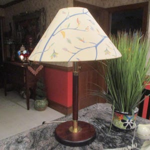 May include: A table lamp with a white lampshade featuring a blue and yellow floral design. The lamp has a brown wooden base and a gold metal accent.