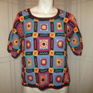 May include: A colorful crocheted top with a geometric pattern of squares in shades of blue, purple, red, yellow, orange, and black.