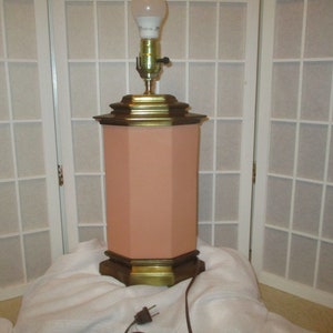 May include: A peach-coloured table lamp with a gold base and a white lampshade. The lamp is sitting on a white surface.