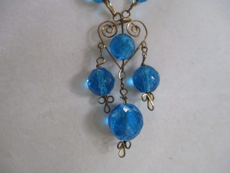 May include: A blue glass bead necklace with a heart-shaped wire design and dangling beads.