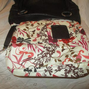 May include: Black leather handbag with a floral patterned interior. The interior fabric features a white background with red, pink, and brown floral designs. A dark brown leather patch is sewn inside the bag.