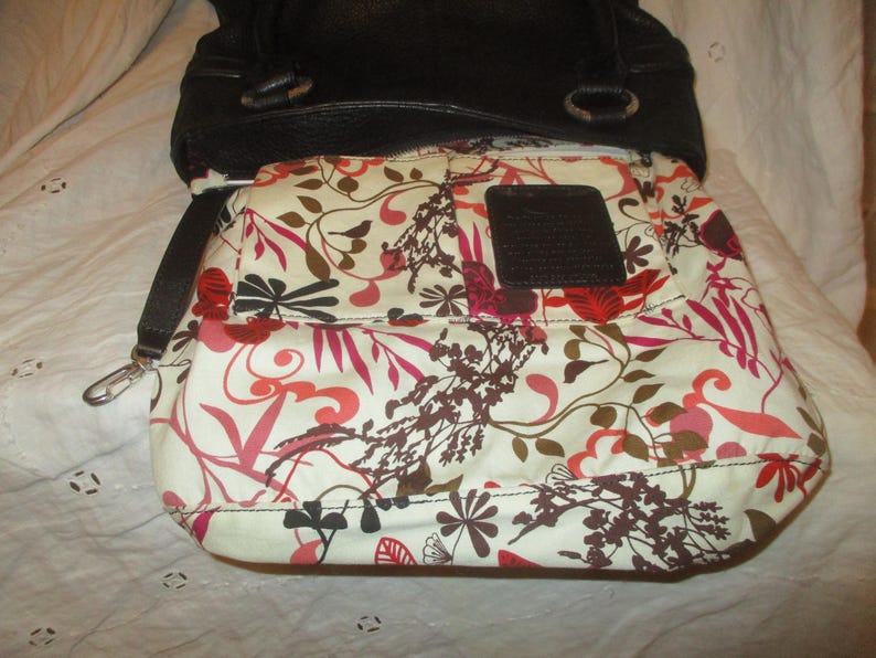 May include: Black leather handbag with a floral patterned interior. The interior fabric features a white background with red, pink, and brown floral designs. A dark brown leather patch is sewn inside the bag.