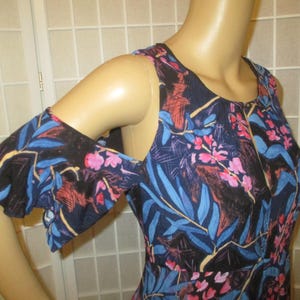 May include: A blue and black floral print cold shoulder dress with a ruffled sleeve. The dress has a scoop neck and a loose fit.