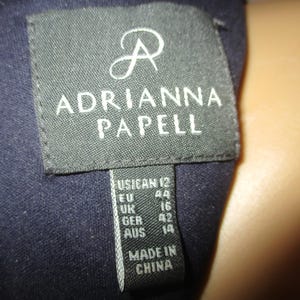 May include: A black label with white text that reads "ADRIANNA PAPELL" and size information: US 12, EU 44, UK 16, GER 42, AUS 14. The label also states "MADE IN CHINA".