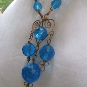 May include: A blue glass bead necklace with a heart-shaped wire pendant and dangling blue glass beads.