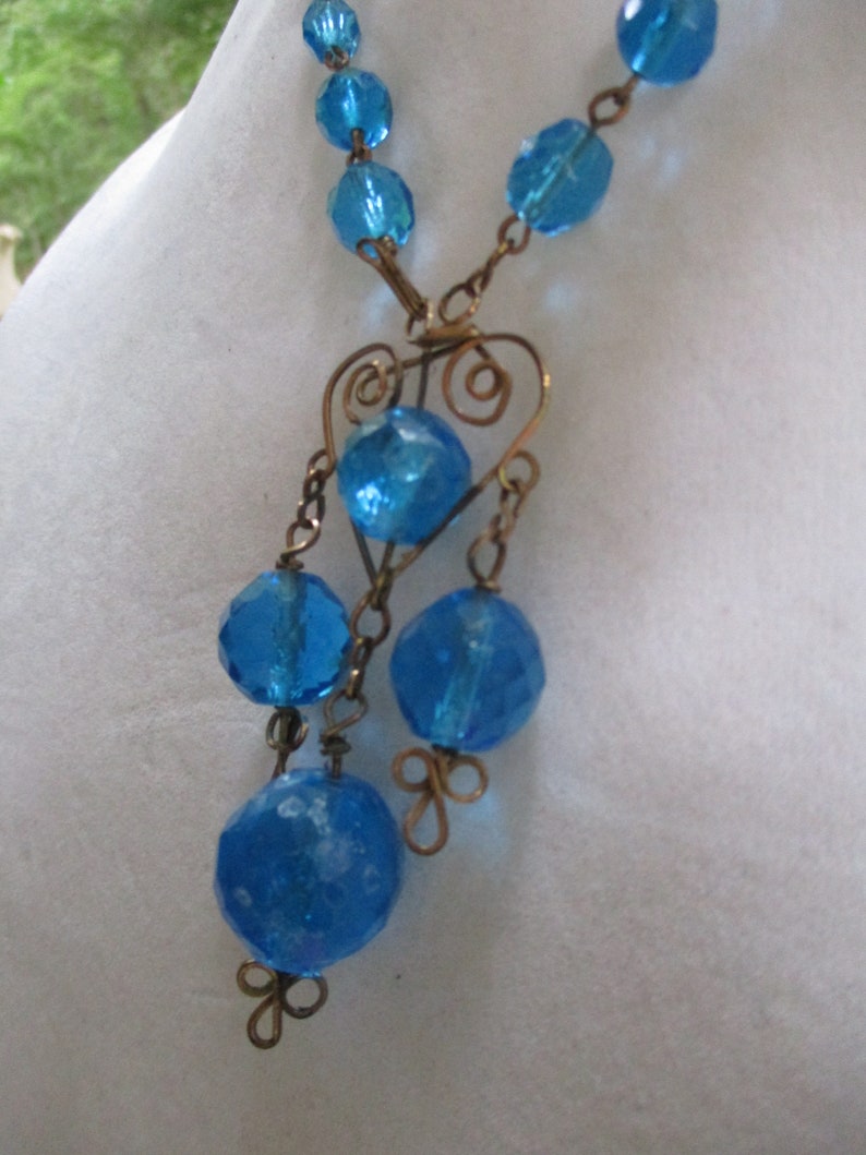 May include: A blue glass bead necklace with a heart-shaped wire pendant and dangling blue glass beads.