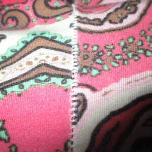 Puede incluir: Primer plano de una tela con un estampado de cachemira. El dise&ntilde;o presenta una combinaci&oacute;n de colores rosa, marr&oacute;n y blanco. La tela est&aacute; dividida por una costura blanca. El estampado de cachemira incluye formas florales y abstractas.