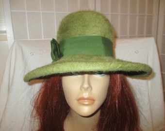 May include: A green fuzzy hat with a wide brim and a green satin ribbon. The hat has a green flower accent on the side.