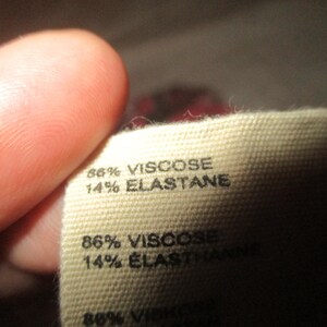Puede incluir: Primer plano de una etiqueta de tela que indica la composici&oacute;n del material. La etiqueta es de color beige y presenta el texto "86% VISCOSE, 14% ELASTANE" en negro. Otra l&iacute;nea de texto dice "86% VISCOSE, 14% ELASTHANNE".