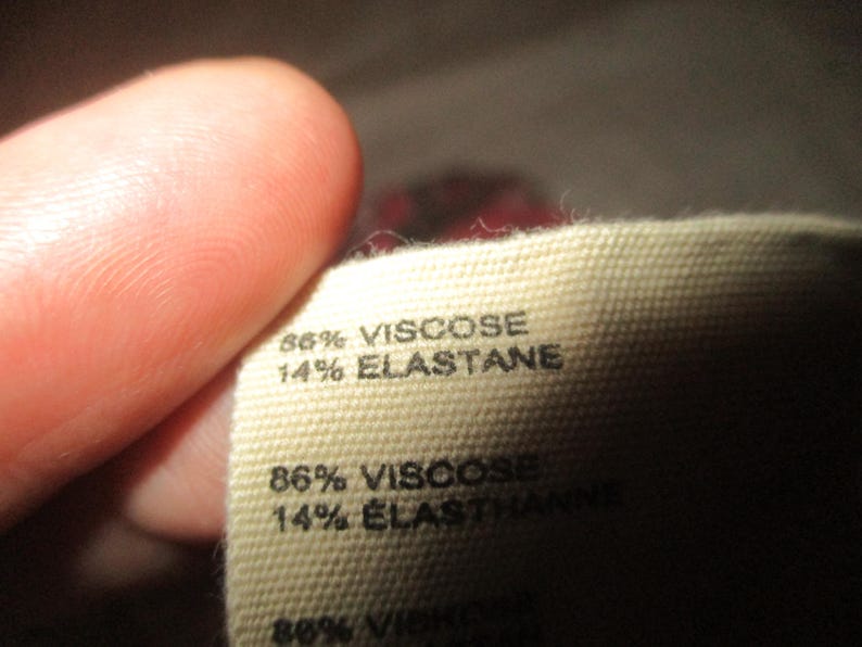 Puede incluir: Primer plano de una etiqueta de tela que indica la composici&oacute;n del material. La etiqueta es de color beige y presenta el texto "86% VISCOSE, 14% ELASTANE" en negro. Otra l&iacute;nea de texto dice "86% VISCOSE, 14% ELASTHANNE".