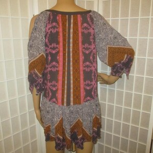 May include: A patterned dress with a scoop neck and three-quarter sleeves. The dress features a mix of colors, including brown, pink, and gray, with a geometric design. The sleeves have an open shoulder design.