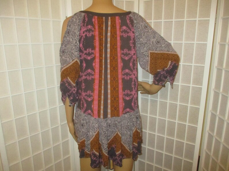 May include: A patterned dress with a scoop neck and three-quarter sleeves. The dress features a mix of colors, including brown, pink, and gray, with a geometric design. The sleeves have an open shoulder design.