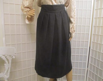 May include: A dark gray, knee-length skirt with a high waist and pleats. The skirt is made of a solid, opaque fabric. The skirt is part of a vintage clothing collection.