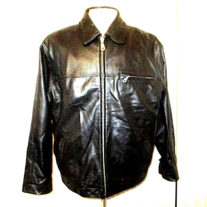 Pode incluir: Casaco de couro preto com gola e fecho de correr. O casaco tem um pequeno bolso com zíper no peito e mangas compridas. É apresentado sobre um fundo branco.