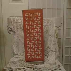 May include: A tall, orange lamp with a geometric pattern cut out of the metal. The lamp has a white cord and plug.