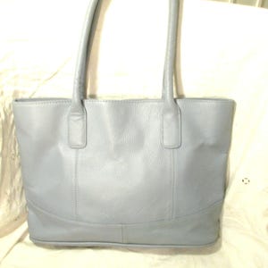 May include: A pale blue leather tote bag with two handles. The bag has a rectangular shape with a curved base and vertical seams. The handles are attached to the top of the bag.