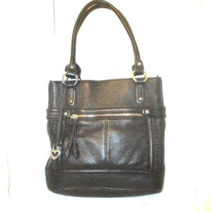 May include: Black leather tote bag with double handles and silver-tone hardware. Features a front zipped pocket, a decorative tassel, and a heart-shaped charm. The bag has a textured finish.