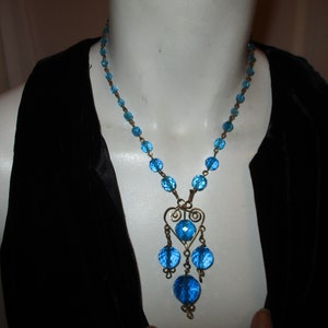 May include: A blue glass bead necklace with a dangling heart-shaped charm. The necklace is made of small, round beads and has a silver-toned metal chain.
