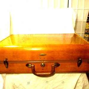 May include: A vintage brown suitcase with a glossy finish. The suitcase has a handle, latches, and a keyhole. The corners are rounded, and the design suggests a classic travel accessory. The suitcase is likely made of leather or a similar material.