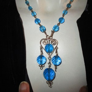 May include: A blue glass bead necklace with a wire heart pendant and dangling blue glass beads.