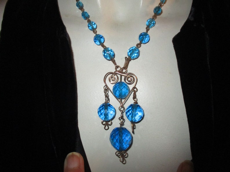 May include: A blue glass bead necklace with a wire heart pendant and dangling blue glass beads.