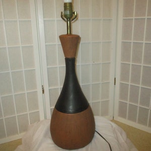 May include: A mid-century modern table lamp with a brown and black ceramic base. The lamp has a simple design with a rounded shape and a black cord.
