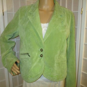 Peut inclure: Un blazer en daim vert clair avec une fermeture à deux boutons et un revers cranté. Le blazer a deux poches avant et des broderies décoratives sur l'ourlet inférieur. Les manches sont longues et la veste est présentée sur un mannequin.