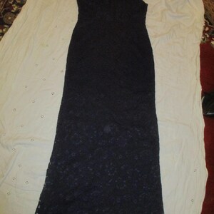 May include: A long, sleeveless, black lace dress with a scalloped hem.