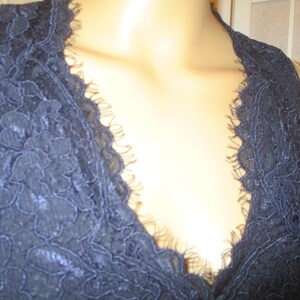 May include: A close-up of a navy blue lace fabric with a deep V-neckline. The lace has a delicate floral pattern.