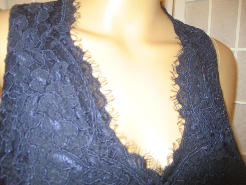 May include: A close-up of a navy blue lace fabric with a deep V-neckline. The lace has a delicate floral pattern.