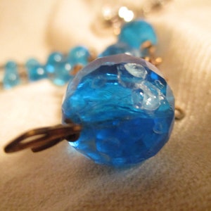 May include: A close-up of a blue glass bead necklace with a textured surface. The beads are connected by silver metal clasps.