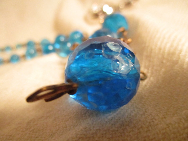 May include: A close-up of a blue glass bead necklace with a textured surface. The beads are connected by silver metal clasps.
