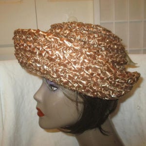 Op de afbeelding: Een vintage, getextureerde, geweven hoed in een warme, metallic bronzen kleur. De hoed heeft een ronde kroon en een licht opstaande rand. De hoed wordt getoond op een mannequinhoofd met donker haar en rode lippenstift.