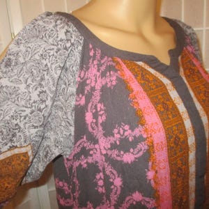 May include: A gray top with a scoop neckline and long sleeves. The sleeves have a gray floral pattern and a split at the shoulder. The front of the top has a pink floral pattern and orange stripes.