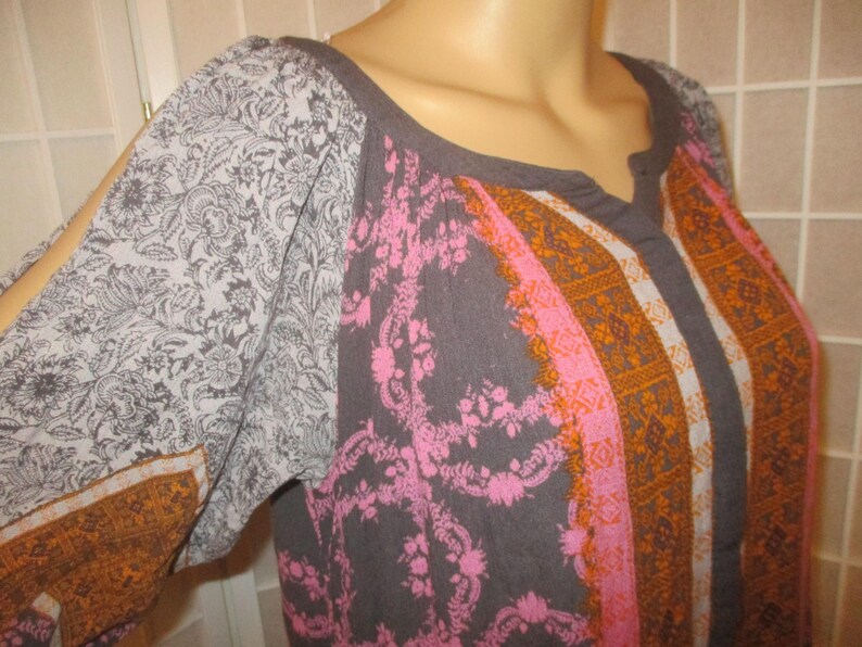 May include: A gray top with a scoop neckline and long sleeves. The sleeves have a gray floral pattern and a split at the shoulder. The front of the top has a pink floral pattern and orange stripes.