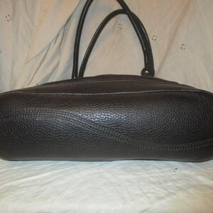 May include: A black leather handbag with a textured finish. The bag features two handles and white stitching. The oval-shaped bag is shown from the bottom.
