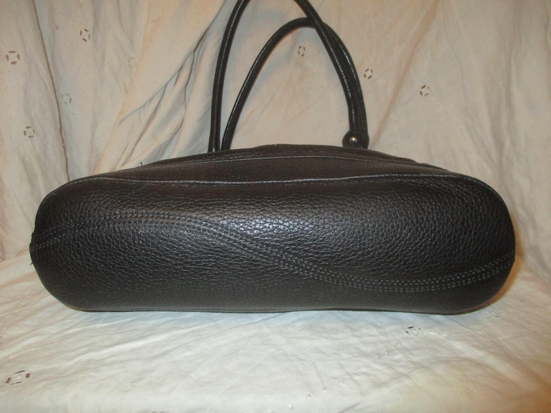 May include: A black leather handbag with a textured finish. The bag features two handles and white stitching. The oval-shaped bag is shown from the bottom.