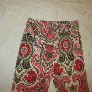 Puede incluir: Primer plano de unas mallas estampadas. Las mallas presentan un dise&ntilde;o de cachemira repetido en tonos rojos, rosas, marrones y verdes. La tela parece suave y c&oacute;moda, adecuada para ropa informal.