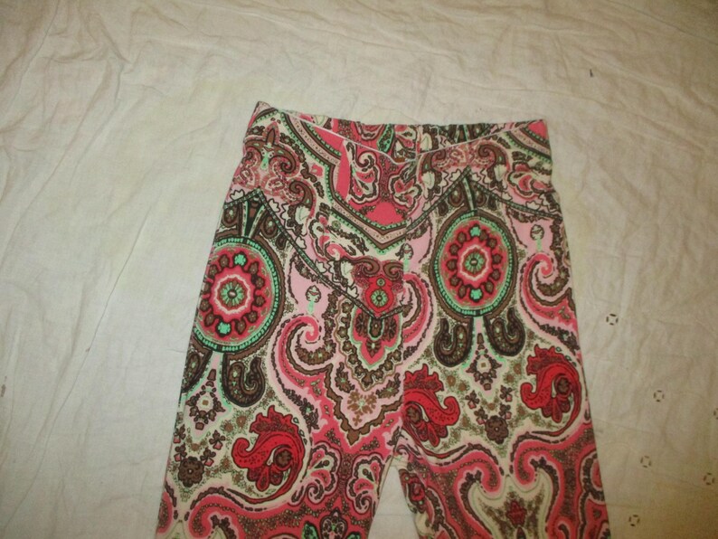 Puede incluir: Primer plano de unas mallas estampadas. Las mallas presentan un dise&ntilde;o de cachemira repetido en tonos rojos, rosas, marrones y verdes. La tela parece suave y c&oacute;moda, adecuada para ropa informal.