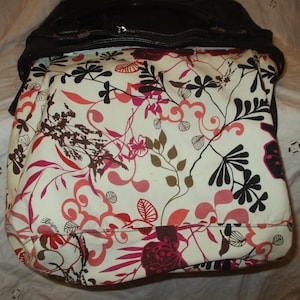 May include: A black handbag with a floral design. The bag's interior has a cream-coloured fabric with a vibrant pattern of red, pink, brown, and black floral and leaf motifs. The bag is open, showing the patterned lining.