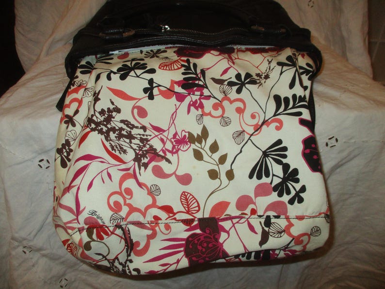 May include: A black handbag with a floral design. The bag's interior has a cream-coloured fabric with a vibrant pattern of red, pink, brown, and black floral and leaf motifs. The bag is open, showing the patterned lining.
