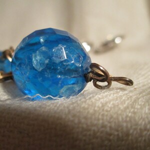 May include: A close-up of a blue glass bead with a textured surface. The bead is attached to a metal clasp.