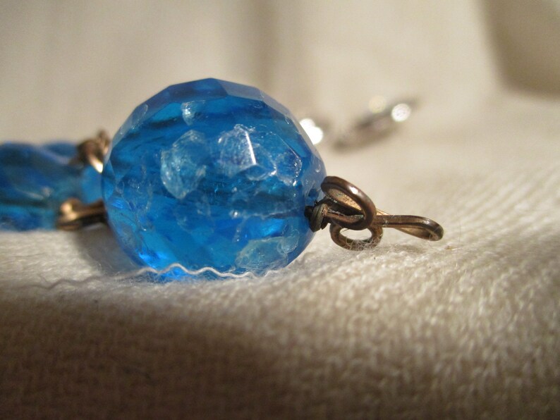 May include: A close-up of a blue glass bead with a textured surface. The bead is attached to a metal clasp.