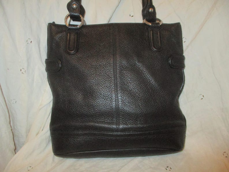 May include: Black leather tote bag with double handles and silver-tone metal rings. The bag has a textured surface and a rectangular shape with a structured design. Features include a top handle and side buckle details.