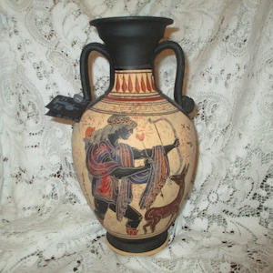 May include: A black and white ceramic vase with a scene of a figure with a bow and arrow hunting a deer. The vase has a black top and red and white accents.