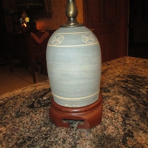 May include: A blue ceramic lamp with a brass base and a wooden stand. The lamp has a white floral design and the text "Ella Capps" on the base.