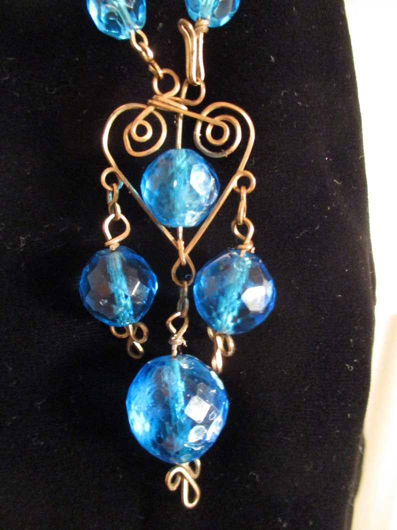 May include: A blue glass bead necklace with a gold wire heart pendant and dangling blue glass beads.