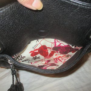 May include: Black leather handbag with silver-tone detailing. The interior has a floral print lining in red, pink, and cream. The bag features a top handle and a decorative tassel.